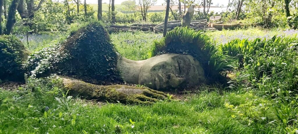 sculpture of a sleeping woman in the ground in a woodland