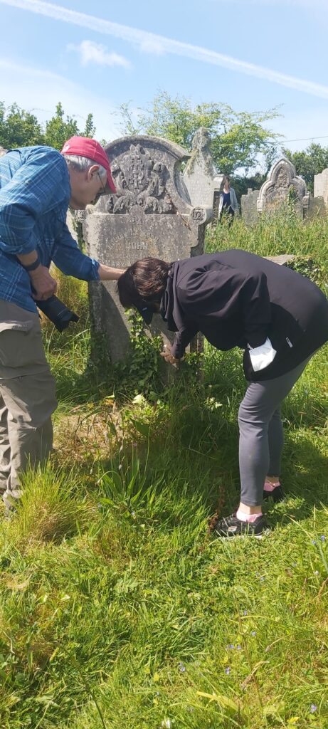two humans crouch to examine a Cornish gravestone
