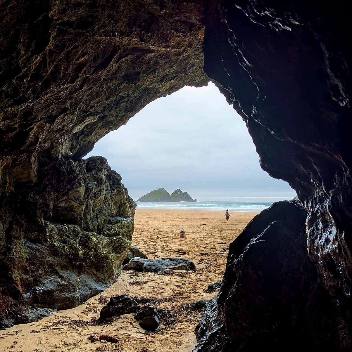 A view of Gull Islands in the sea seen out of a cave across a beach with a dog and human figure in the distance