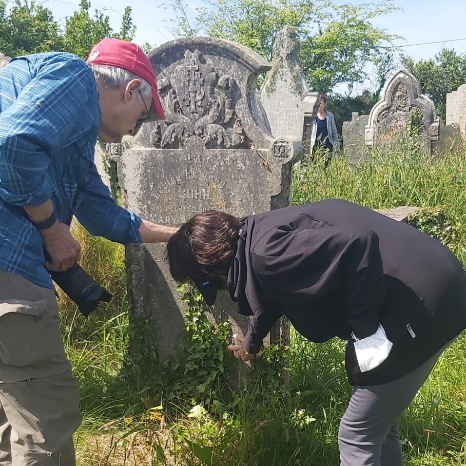 two humans crouch to examine a Cornish gravestone